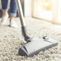 Cropped image of beautiful young woman using a vacuum cleaner while cleaning carpet in the house